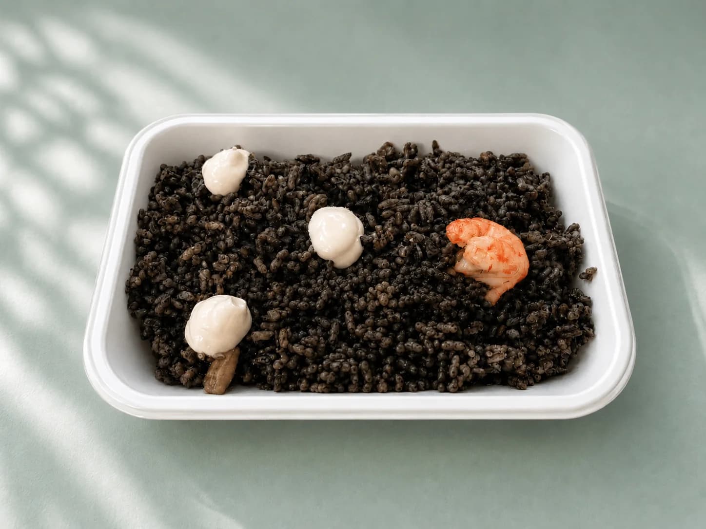 Arroz negro con gambas preparado para llevar en una bandeja blanca